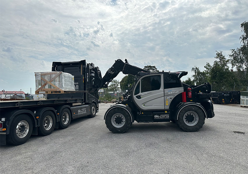 Företagets svartlackerade lastbil har lastväxlare och kan transportera företagets maskiner när det blir för långt att hjula, eller som här köra ut material till arbetsplatserna.